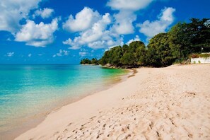 A beach with clear turquoise water, sandy shore, and dense green foliage in the background.