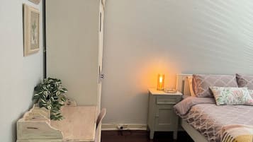 A bedroom with a bed, a nightstand, a dresser, a lamp, and an air conditioner.