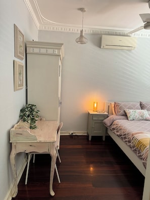 A bedroom with a bed, a nightstand, a dresser, a lamp, and an air conditioner.
