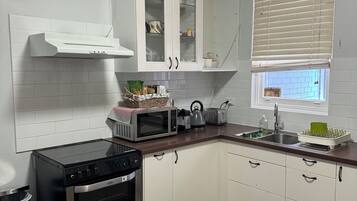 A modern kitchen with white cabinets, a built-in oven, a microwave, and a window with blinds.