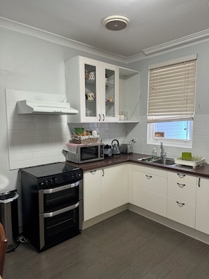 A modern kitchen with white cabinets, a built-in oven, a microwave, and a window with blinds.