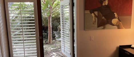 A bedroom with a bed, a painting, and a view through an open door to a garden.