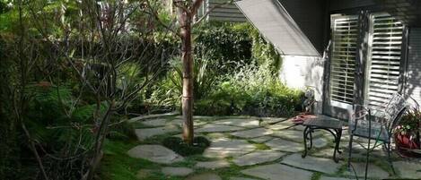 Ein Steinweg führt zu einer Terrasse mit einem Metalltisch und Stühlen.
