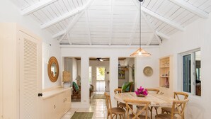 Un comedor con una mesa redonda, sillas de madera, una lámpara colgante y vista a otra habitación.