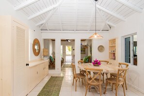 Un comedor con una mesa redonda, sillas de madera, una lámpara colgante y vista a otra habitación.