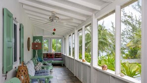 Un porche cubierto con una banca, un ventilador de techo y vistas a la vegetación tropical.
