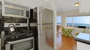 A modern kitchen with stainless steel appliances, a view of the ocean through large windows, and a dining area with green chairs. - Oceanfront Cottage on Carbon Beach -Sea Lion (Malibu)