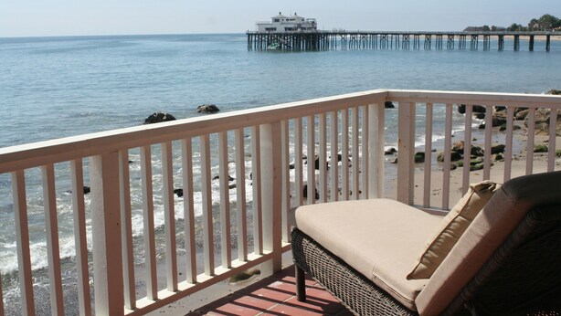 A beach view with a wooden deck, a lounge chair, and a pier in the background. - Oceanfront Cottage on Carbon Beach -Sea Lion (Malibu)
