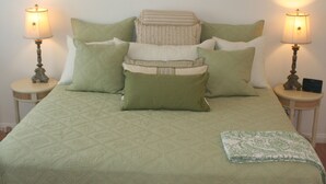 A bed with a quilted green bedspread, multiple pillows, and two bedside lamps on wooden nightstands. - Oceanfront Cottage on Carbon Beach -Sea Lion (Malibu)