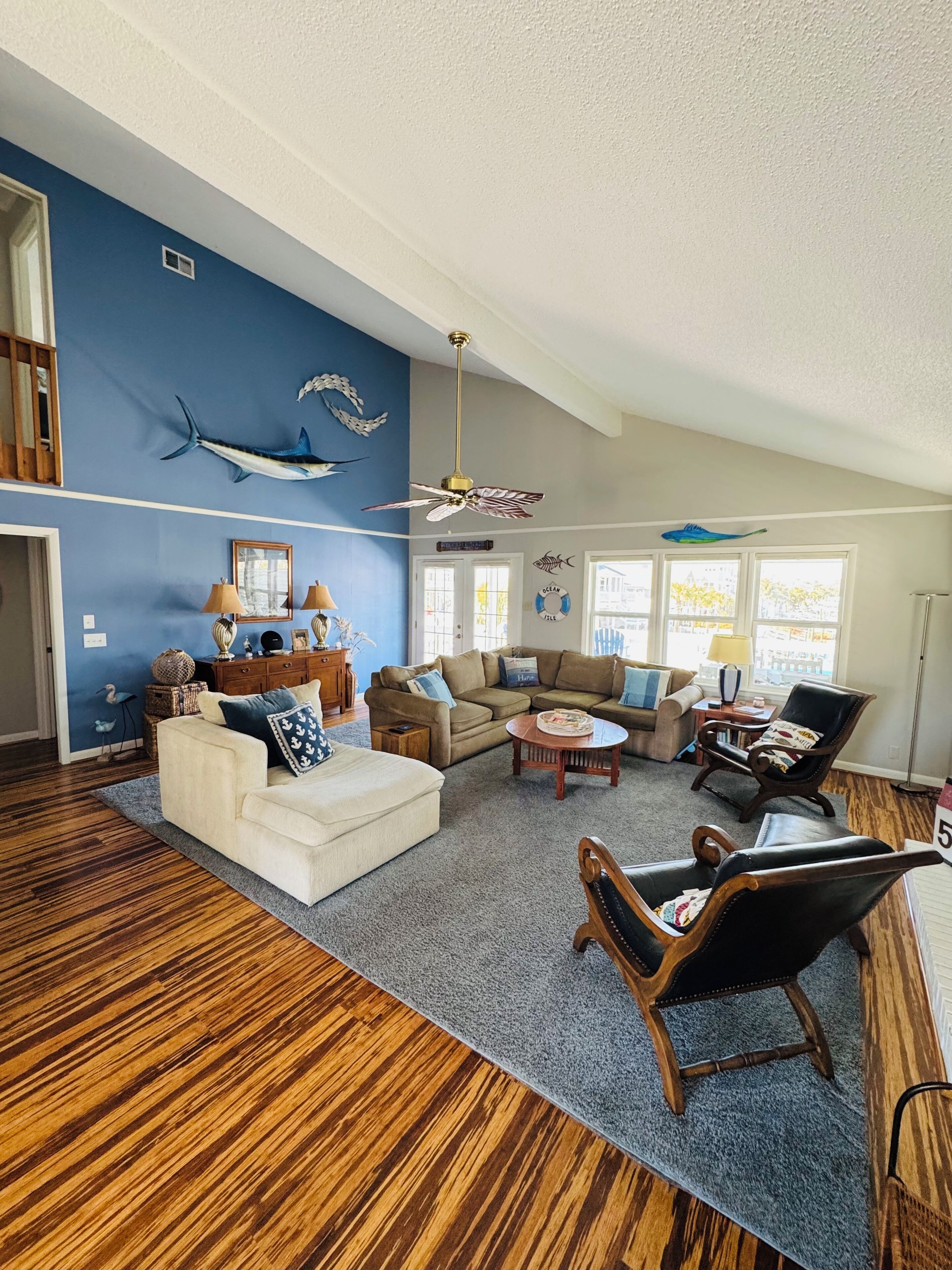 A spacious living room with a blue accent wall, a ceiling fan, and a large window providing natural light.