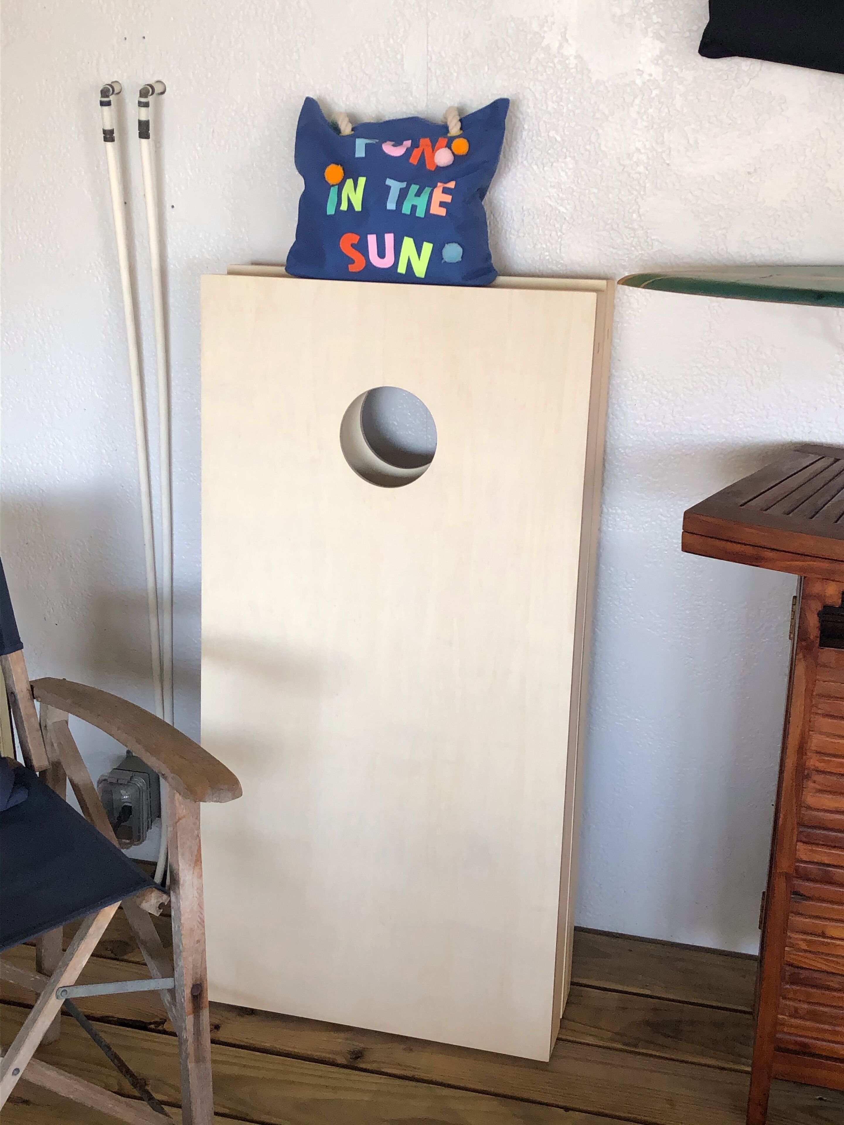 Ein Holzschrank mit einer runden Aussparung, ein blaues Kissen mit bunter Schrift und ein Holzbstuhl.