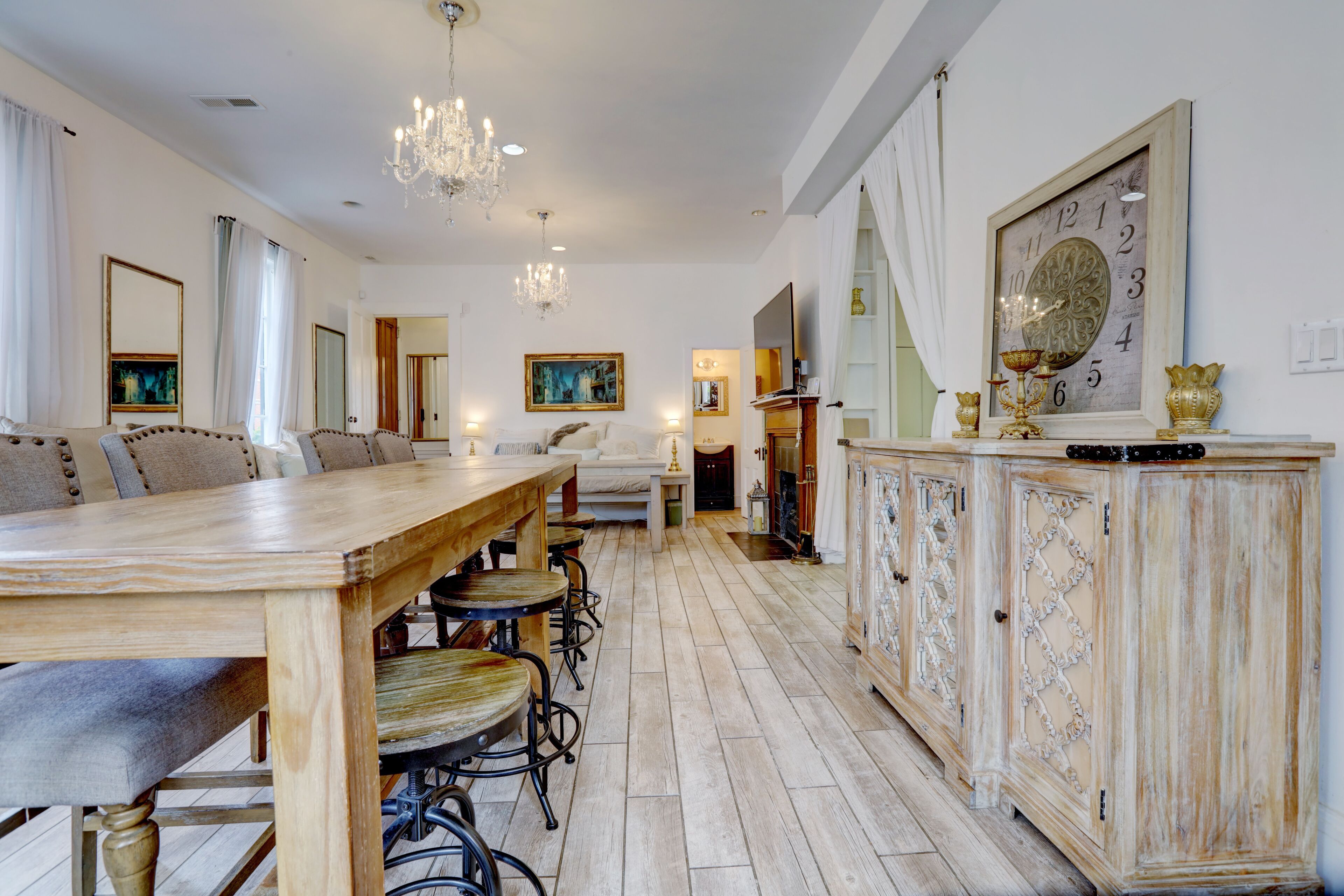 Un comedor amplio con una larga mesa de madera y numerosas sillas, una araña y un aparador decorativo con un reloj.
