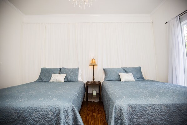 A room with two beds, a nightstand with a lamp, and a window with curtains.