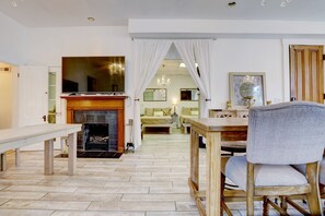 Ein geräumiges Wohnzimmer mit Kamin, großem Fernseher und Essbereich mit Holztisch und Stühlen.