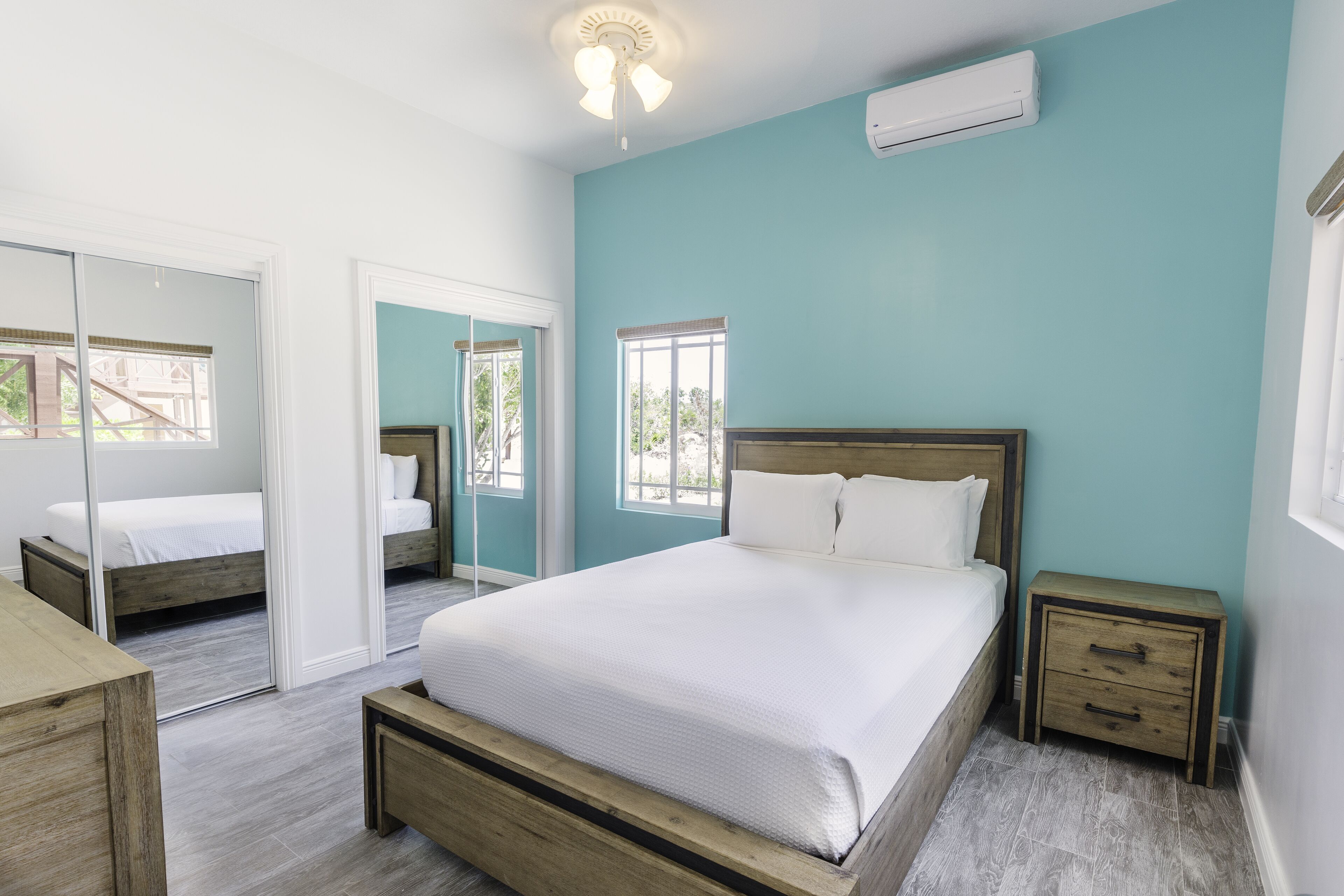 A bedroom with a large bed, a wooden nightstand, a mirror, and a window.