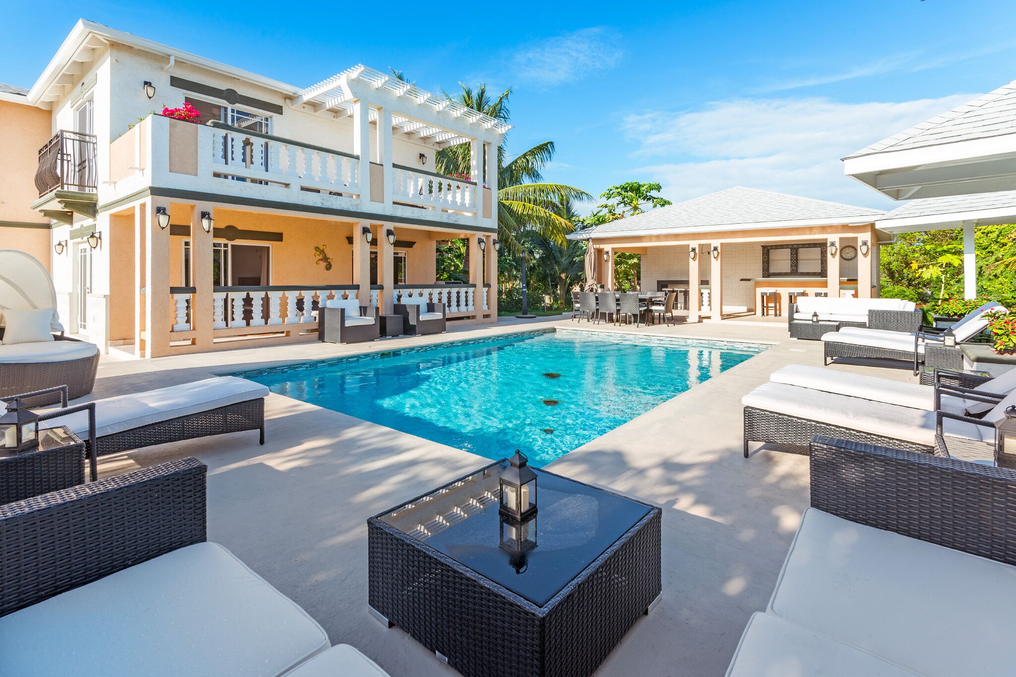 A two-story building with a swimming pool, outdoor seating, and a covered area with a table and chairs.