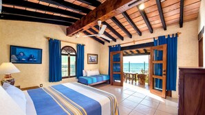 Camera d'albergo con un letto grande, un ventilatore a soffitto e vista sul mare attraverso porte aperte.