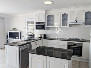 Une cuisine moderne avec des meubles blancs, un plan de travail noir, un four à micro-ondes encastré, une cuisinière à gaz et un lave-vaisselle.