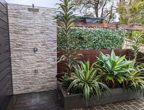 Un mur de pierres agrémenté d’un élément décoratif aquatique, une clôture en bois et un jardinier contenant diverses plantes.