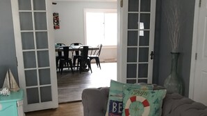 Een woonkamer met een grijze bank, een blauwgroene dressoir en een eethoek op de achtergrond.