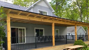 Een overdekte veranda met houten leuning, een bankje en uitzicht op een huis met grijze gevel en witte details.