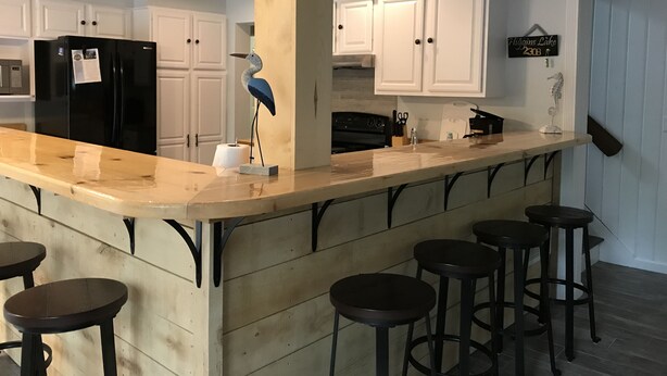 Een keuken met witte kasten, een zwarte koelkast, een houten kookeiland met krukken, en een decoratieve vogelsculptuur.