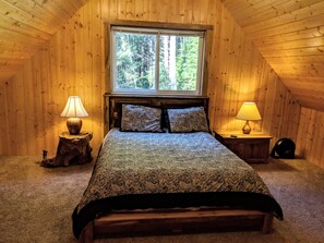 Ein gemütliches Schlafzimmer im Dachgeschoss mit einem großen Bett, zwei Nachttischlampen und einem Fenster mit Blick auf einen Wald.