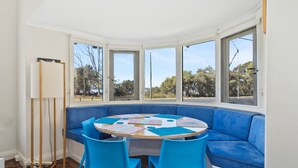 A room with a round table, blue chairs, a blue sofa, and large windows offering a view of trees and a body of water.