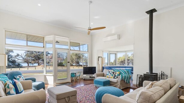 A spacious living room with a large TV, comfortable seating, a fireplace, and large windows offering a view of the outdoors.