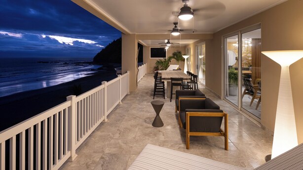 A balcony with a view of the ocean at dusk, featuring a dining area with chairs and a table, a ceiling fan, and a potted plant. - The best condo in Jaco Beach, just got A LOT BETTER!
 (Jaco)