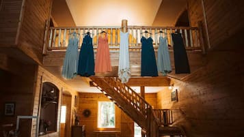 Un intérieur en bois avec un escalier menant à un balcon où sont suspendues des robes.