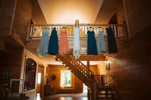 Interior de madeira com escada que leva a uma varanda onde vestidos estão pendurados.