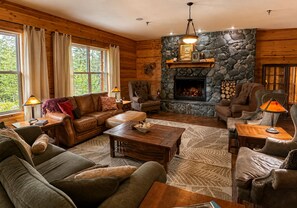 A cozy log cabin interior with a stone fireplace, leather furniture, and a view of the outdoors.