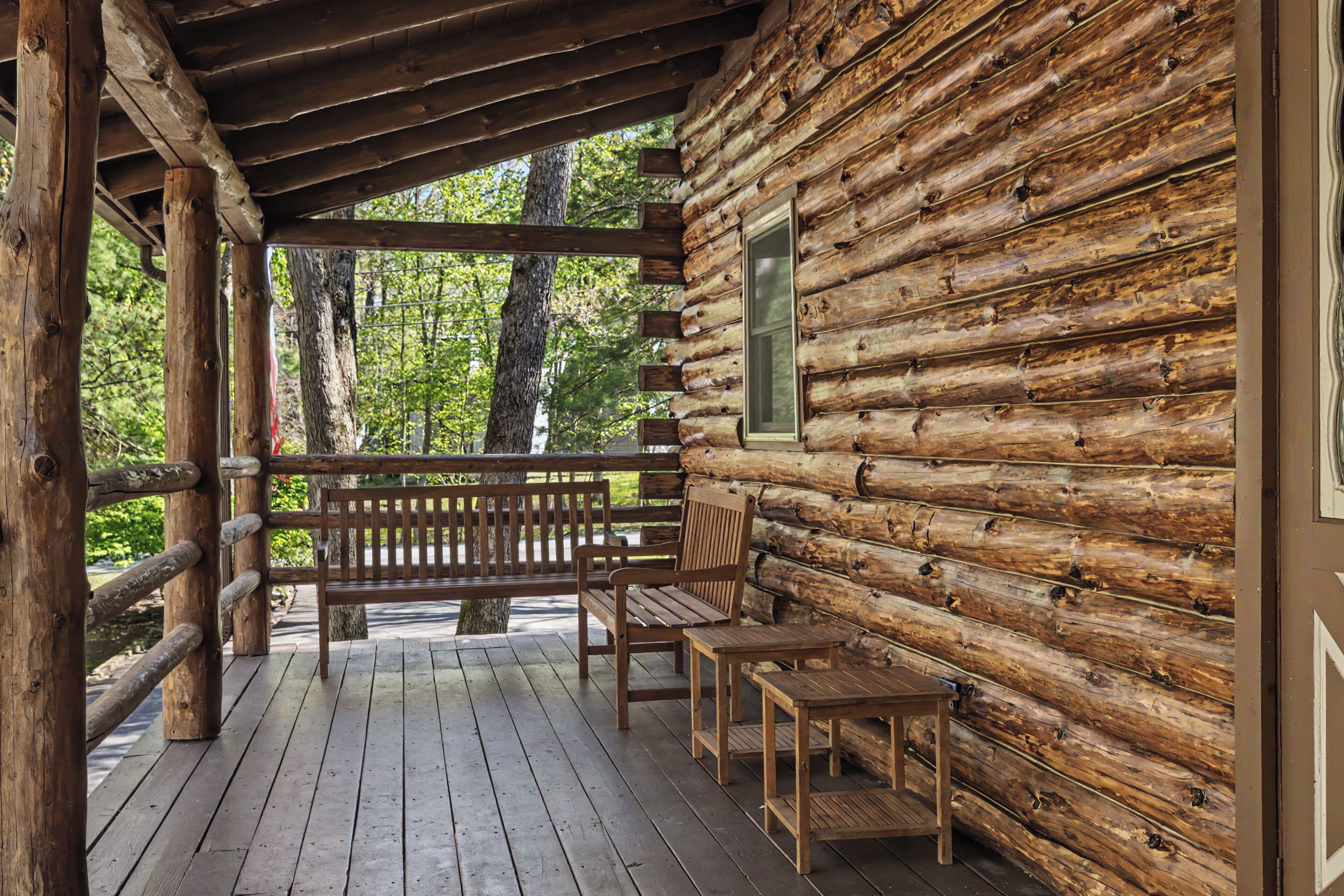 Une cabane en rondins avec une terrasse en bois, deux chaises, une table et une fenêtre.
