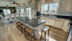 A spacious kitchen with a large island, wooden stools, and a view of the city through large windows. - Down South | 450 ft from the beach | Private Pool (Virginia Beach)