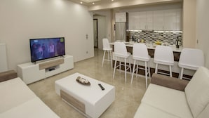 A modern living room with a TV, white sofas, a coffee table, and a kitchen area with white bar stools. - Spacious & Convenient Place near Acropolis Museum by GHH (Athens)