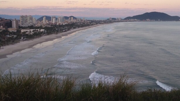 A coastal cityscape with a beach, buildings, and mountains in the background. - Pitangueiras Apartment in Guaruja (Barra Funda)