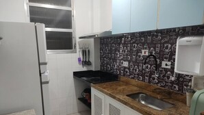 A kitchen with white cabinets, a black backsplash with coffee-themed designs, a stainless steel sink, and a coffee machine. - Pitangueiras Apartment in Guaruja (Barra Funda)