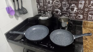 A kitchen with two electric frying pans on a black stovetop, a coffee maker, and a wall with coffee-themed illustrations. - Pitangueiras Apartment in Guaruja (Barra Funda)