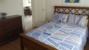 A bedroom with a bed, wooden dresser, and a painting on the wall. - Pitangueiras Apartment in Guaruja (Barra Funda)