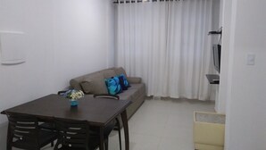 A small, sparsely furnished room with a sofa, a table, and a TV. - Pitangueiras Apartment in Guaruja (Barra Funda)