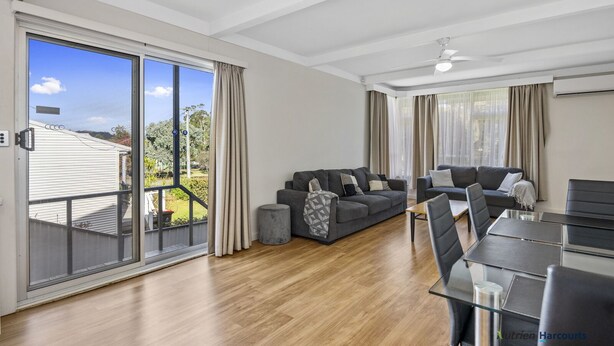 A spacious living area with a sliding glass door leading to a balcony, a grey sofa set, a dining table with chairs, and a ceiling fan. - Room for the whole family (Eildon)