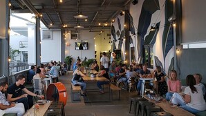 Un comedor interior con mesas y sillas, ventanas amplias y un mural en la pared.