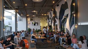 An indoor dining area with tables and chairs, large windows, and a mural on the wall.