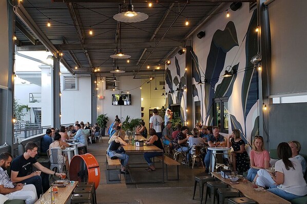 Un comedor interior con mesas y sillas, ventanas amplias y un mural en la pared.