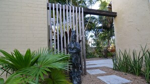 Un jardín con una estatua, un portón de madera y un sendero.