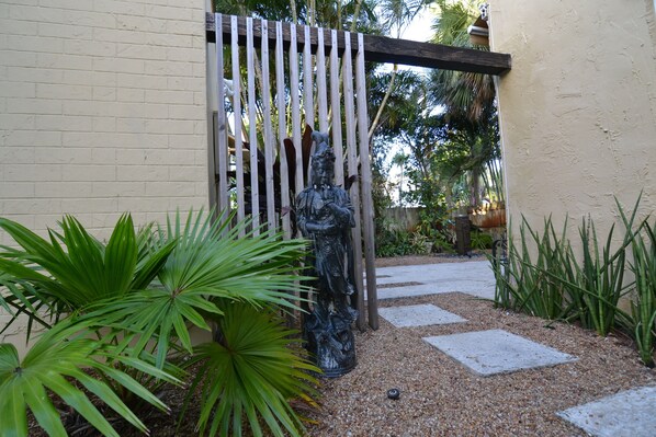 A garden with a statue, a wooden gate, and a pathway.