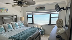 Ein Schlafzimmer mit einem großen Bett, einem Deckenventilator, Meerblick, einem Schreibtisch mit Computer und einem dekorativen Wandbild.