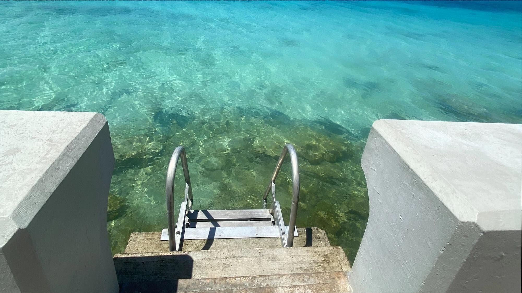 Un escalier en béton menant à une eau turquoise et cristalline.