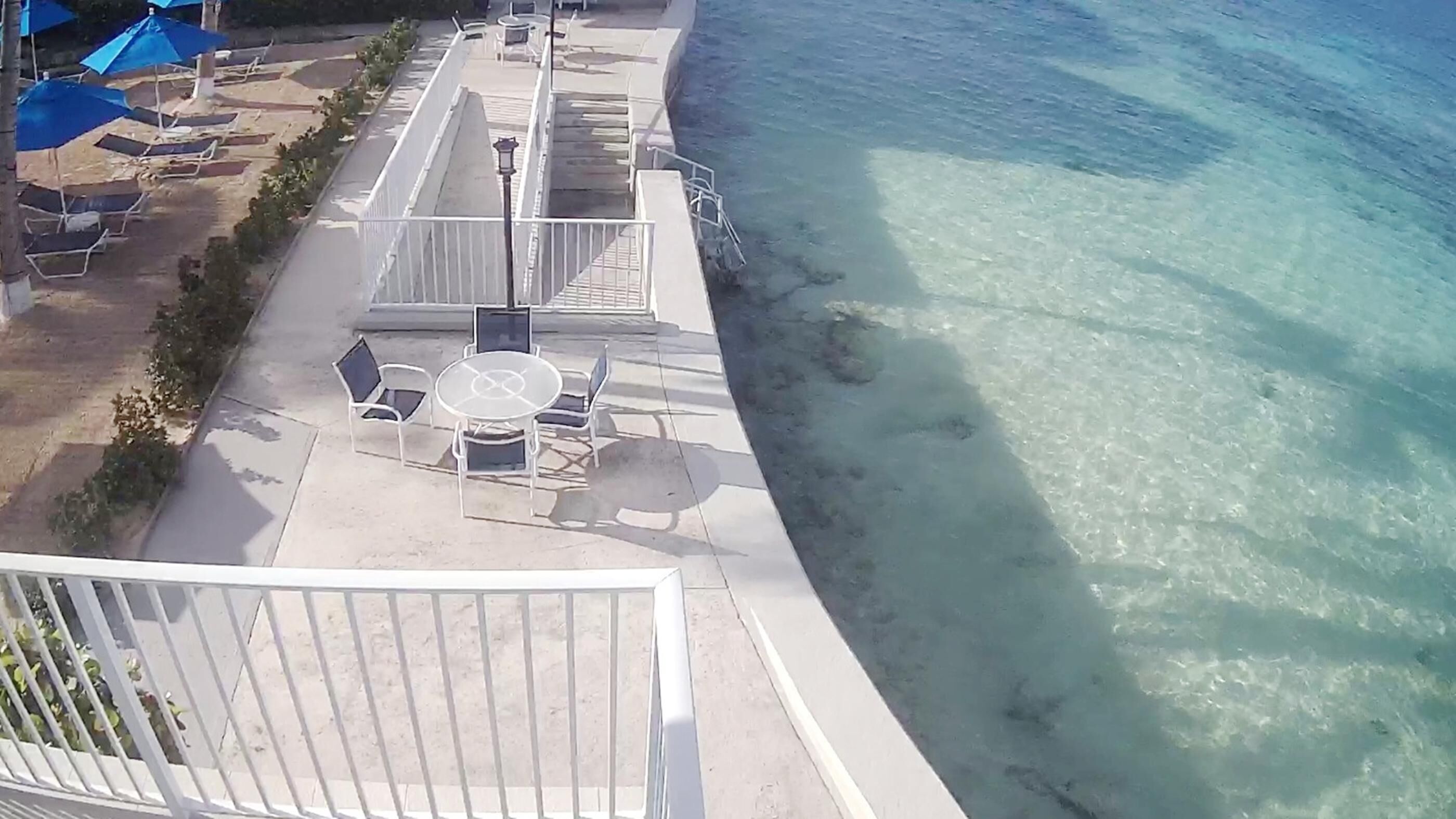 A balcony with a table and chairs overlooking a clear beach.